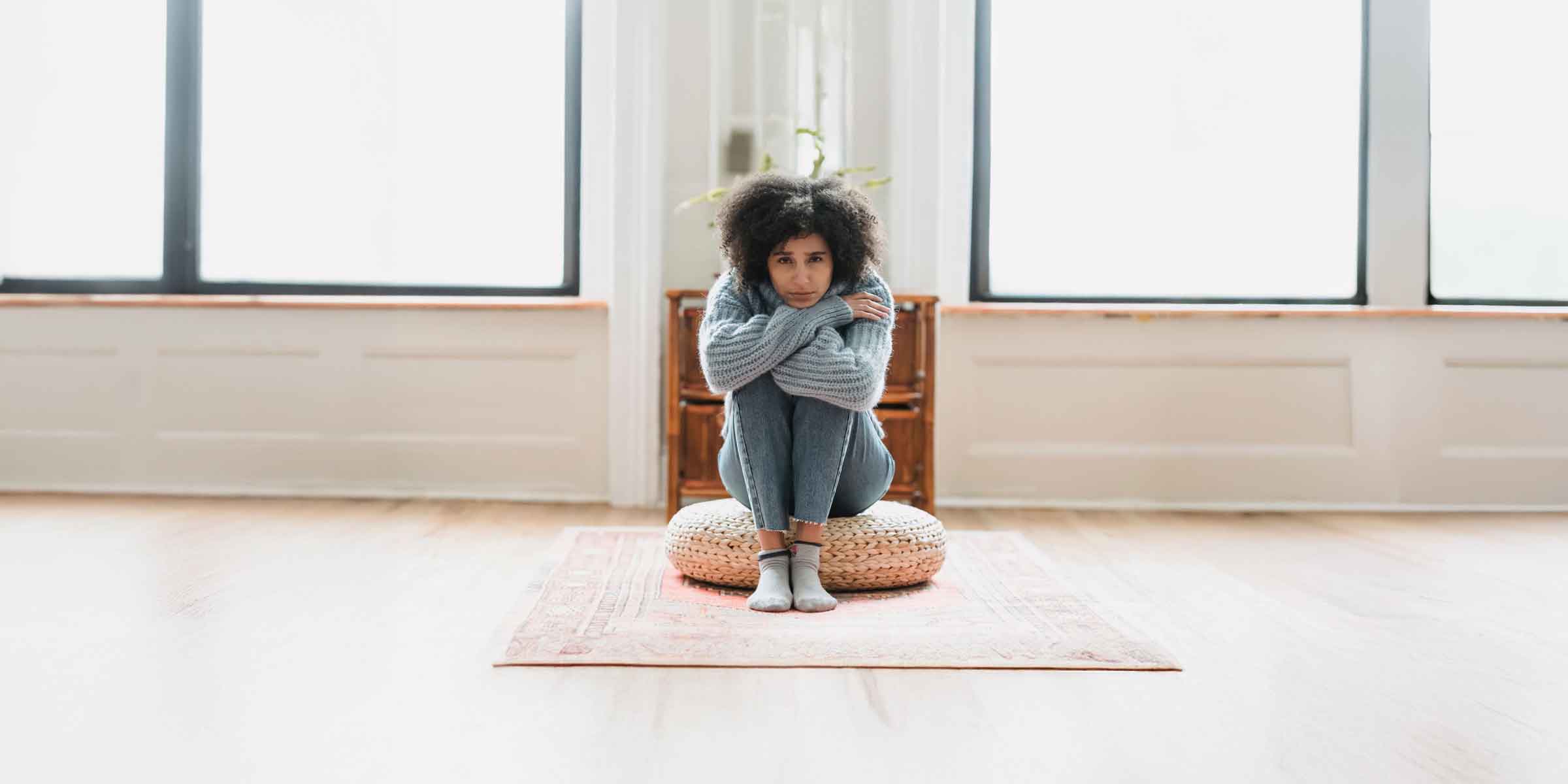 Woman, looking sad, seated on cushion in sunny room