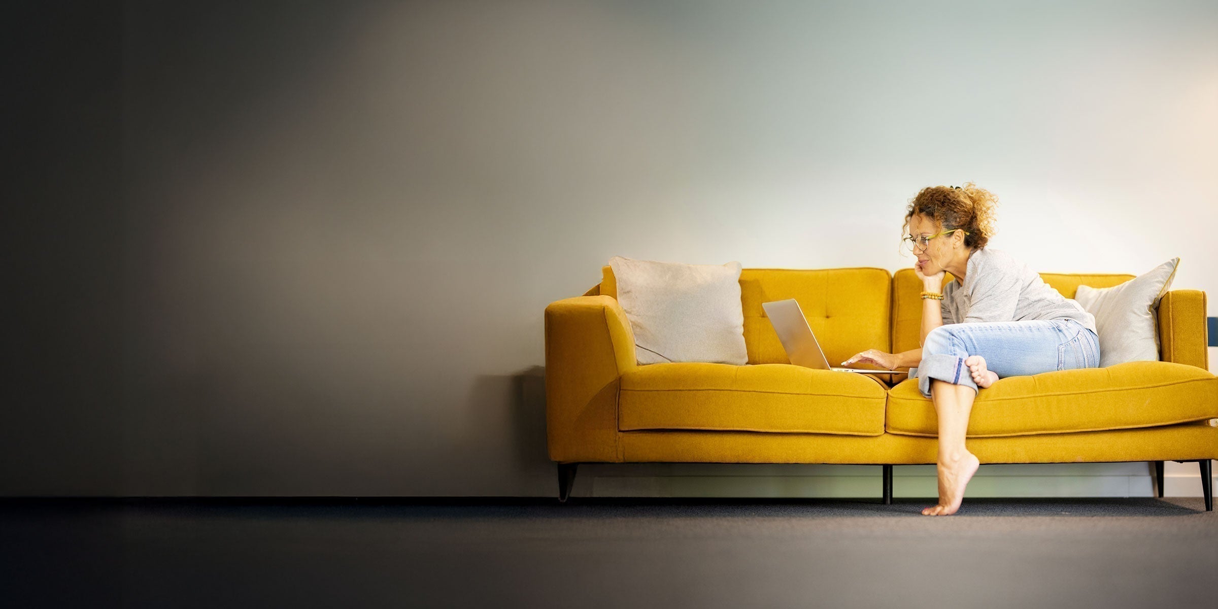 Woman on a yellow sofa looking at her laptop to review kidney lab results and health markers.