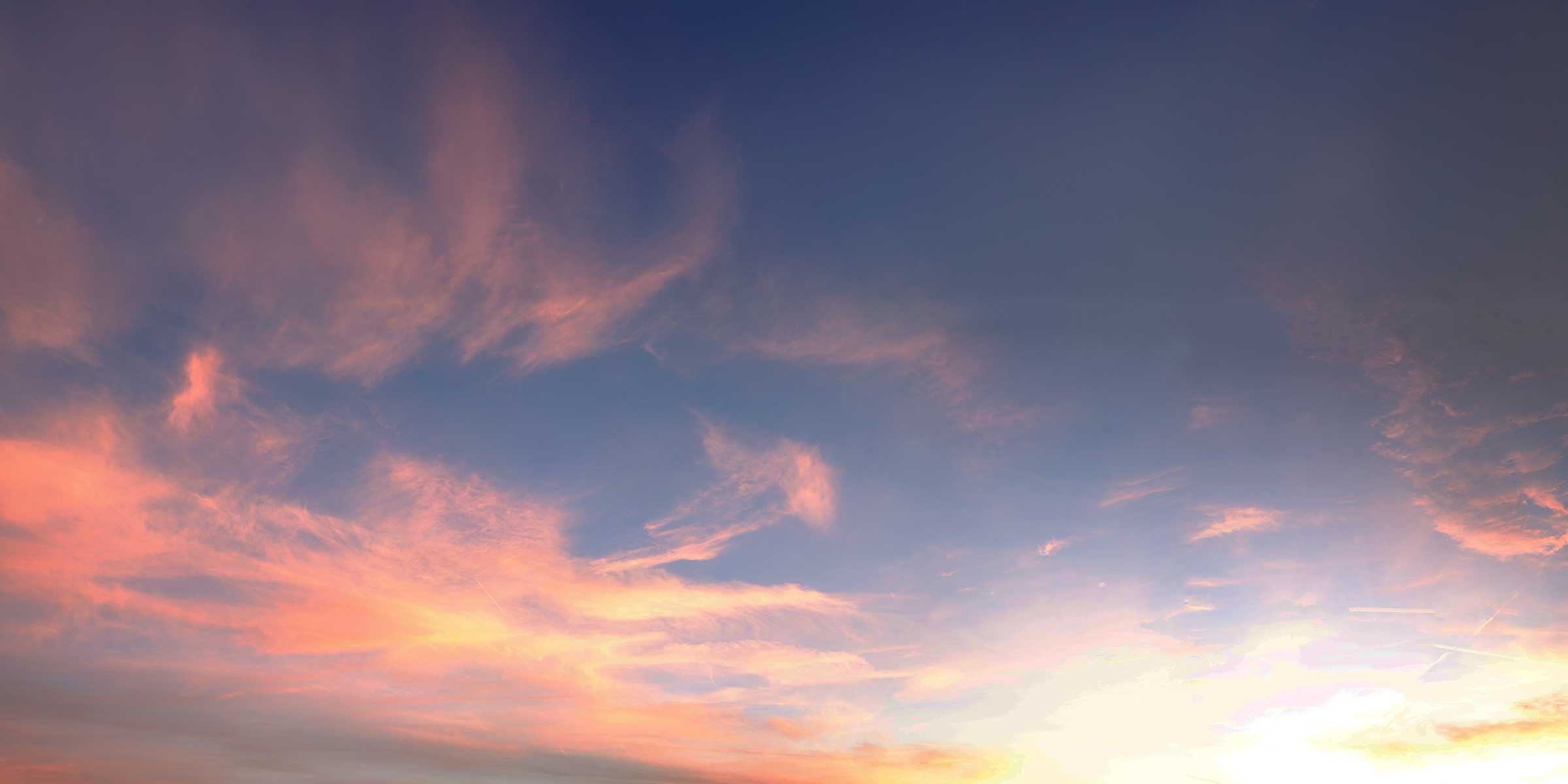 A wide-angle landscape shot of a vibrant sunset or sunrise with orange and blue wispy clouds stretching across the sky.