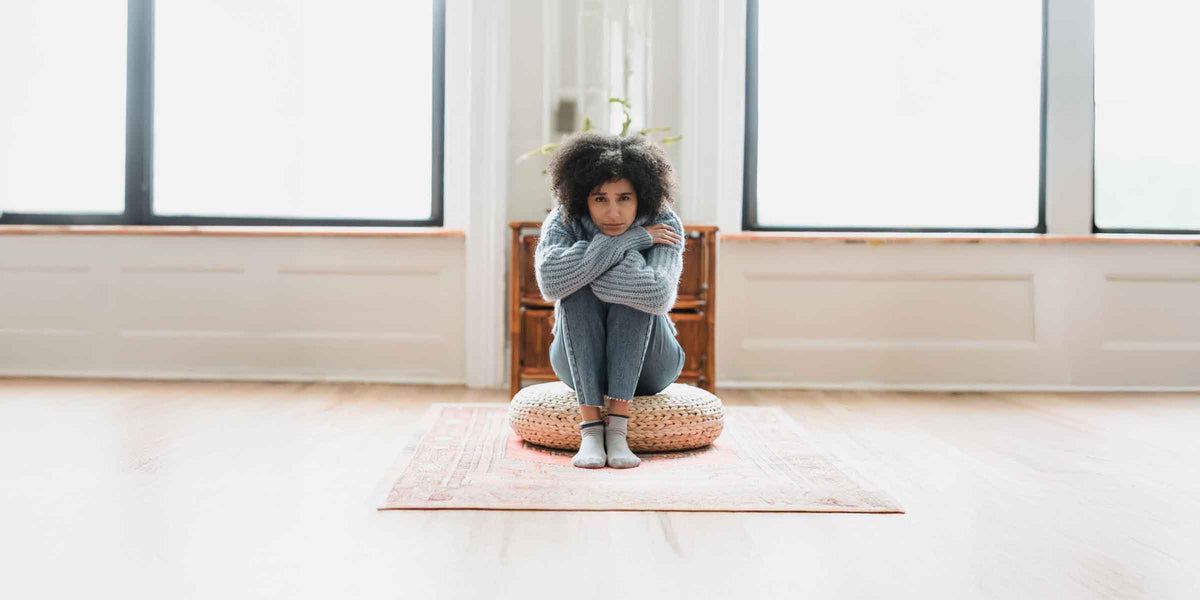 Woman, looking sad, seated on cushion in sunny room