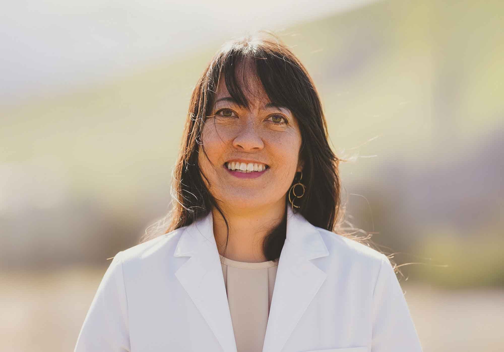 Woman wearing a white lab coat with a blurred outdoor background