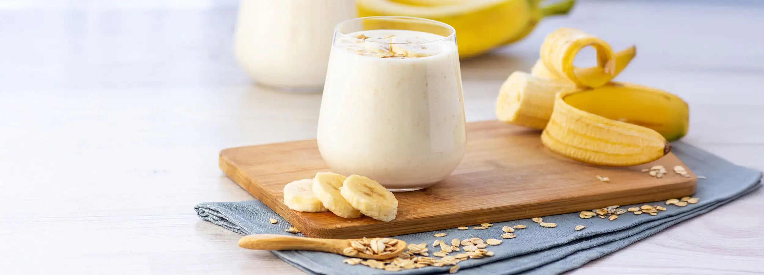 Banana smoothie with oats in a glass on a cutting board with a blue cloth napkin