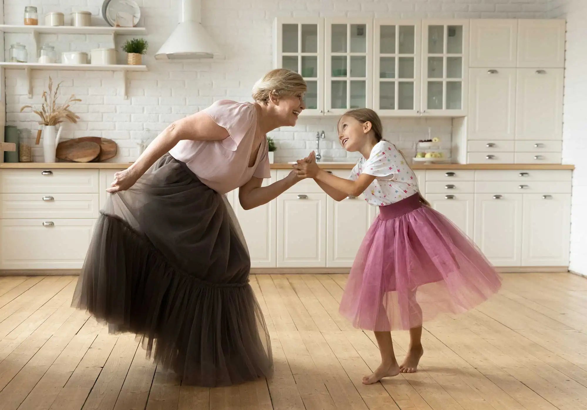 Grandmother and granddaughter dancing in kitchen with tutus on